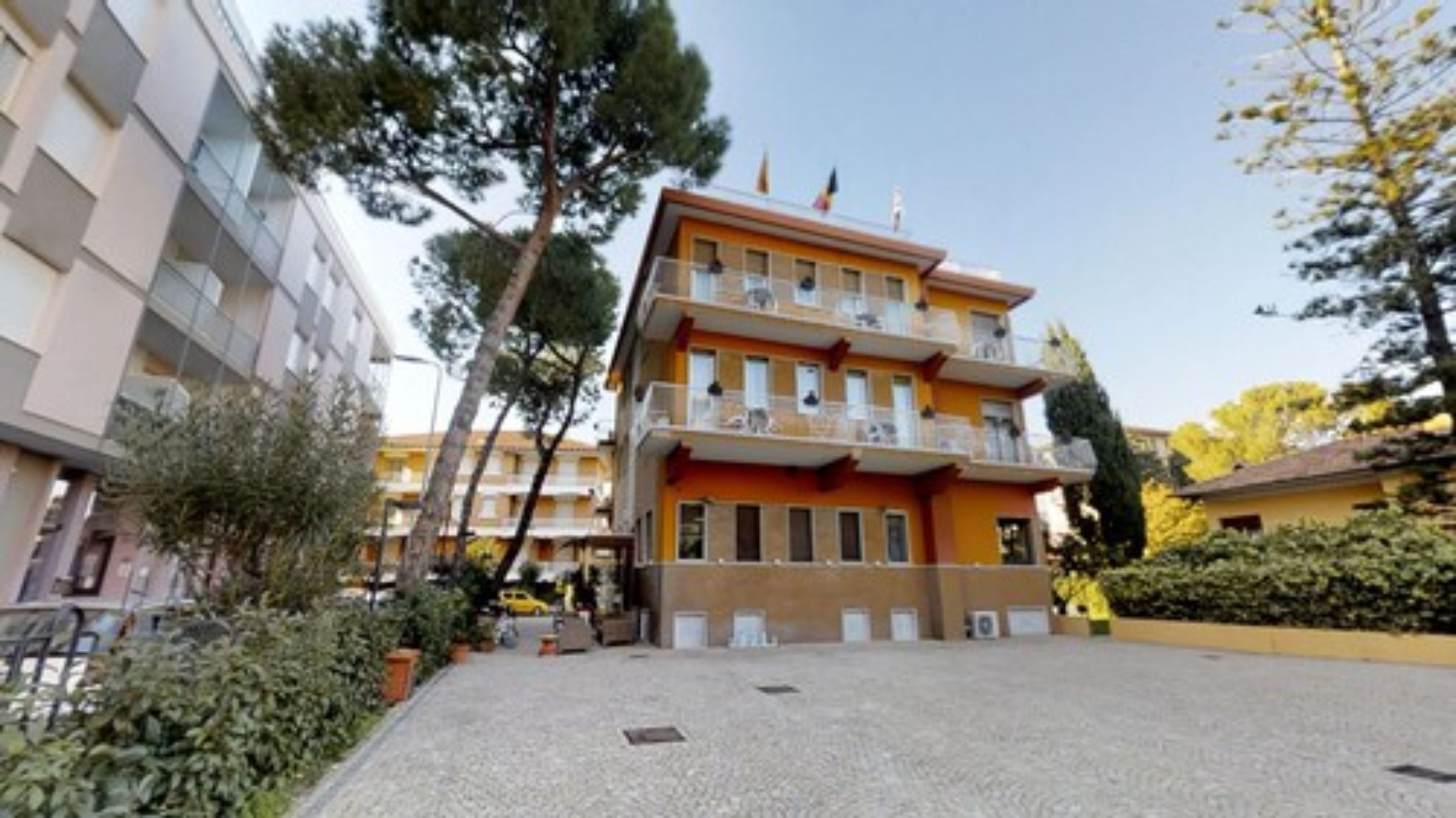 Un immeuble à plusieurs étages doté de balcons, d’une cour en gravier et entouré de verdure.