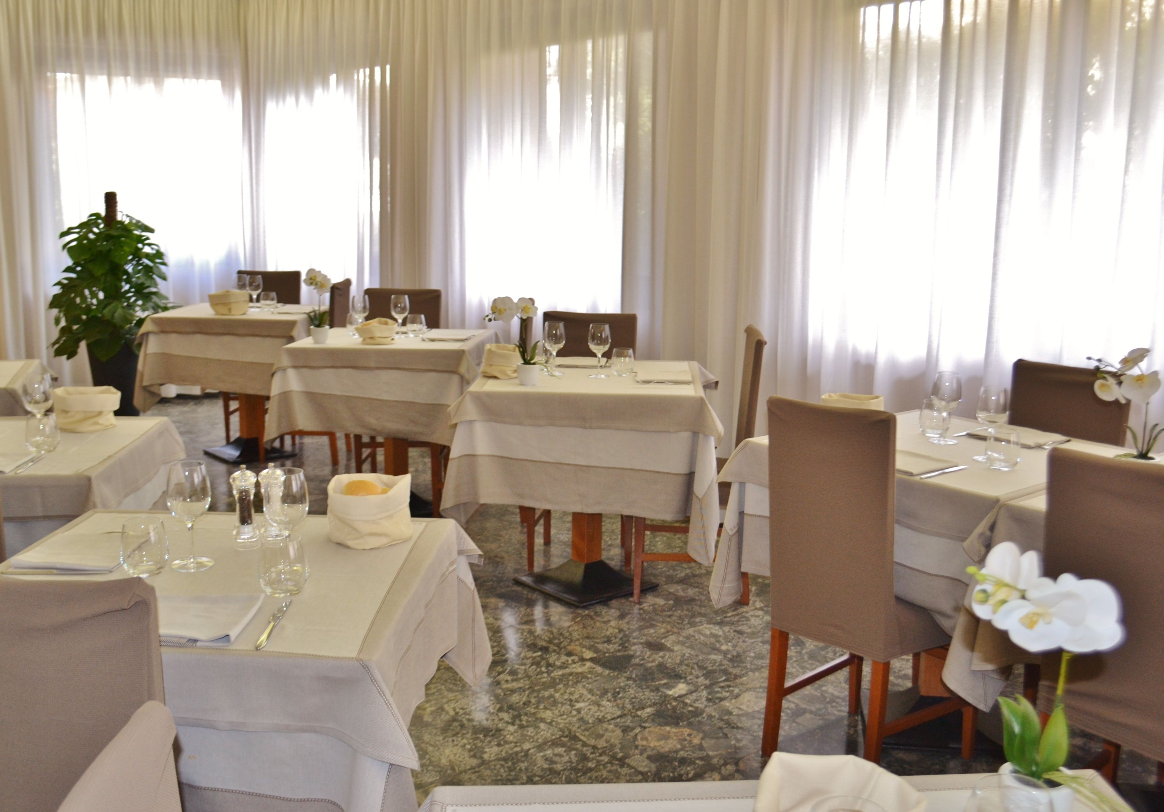 A restaurant with multiple tables, each set with white tablecloths, wine glasses, and chairs.