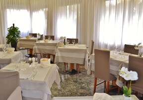 Un restaurante con varias mesas, cada una con manteles blancos, copas de vino y sillas.