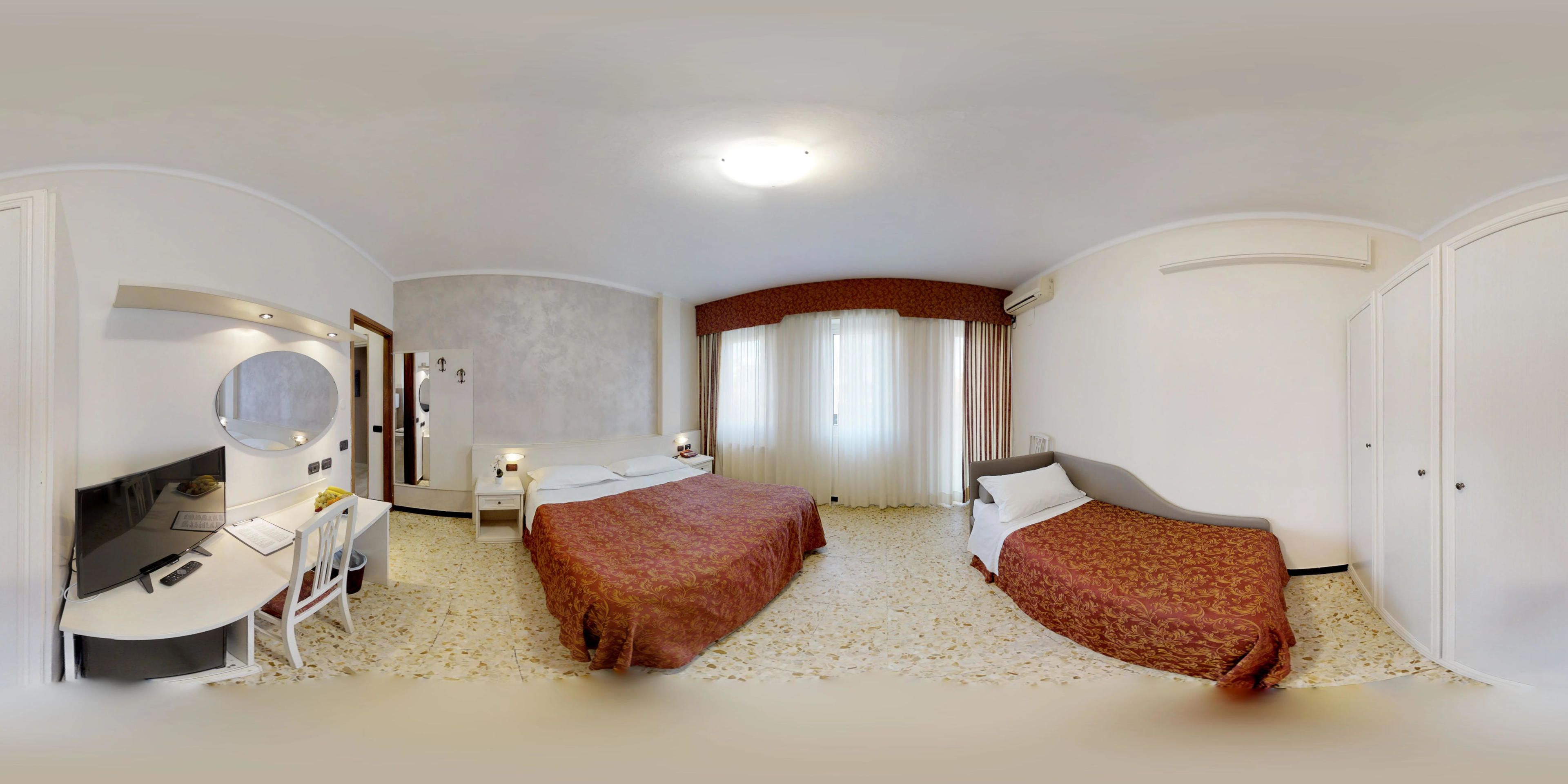 Hotellihuone, jossa on kaksi sänkyä, työpöytä tuolilla, peili ja televisio.