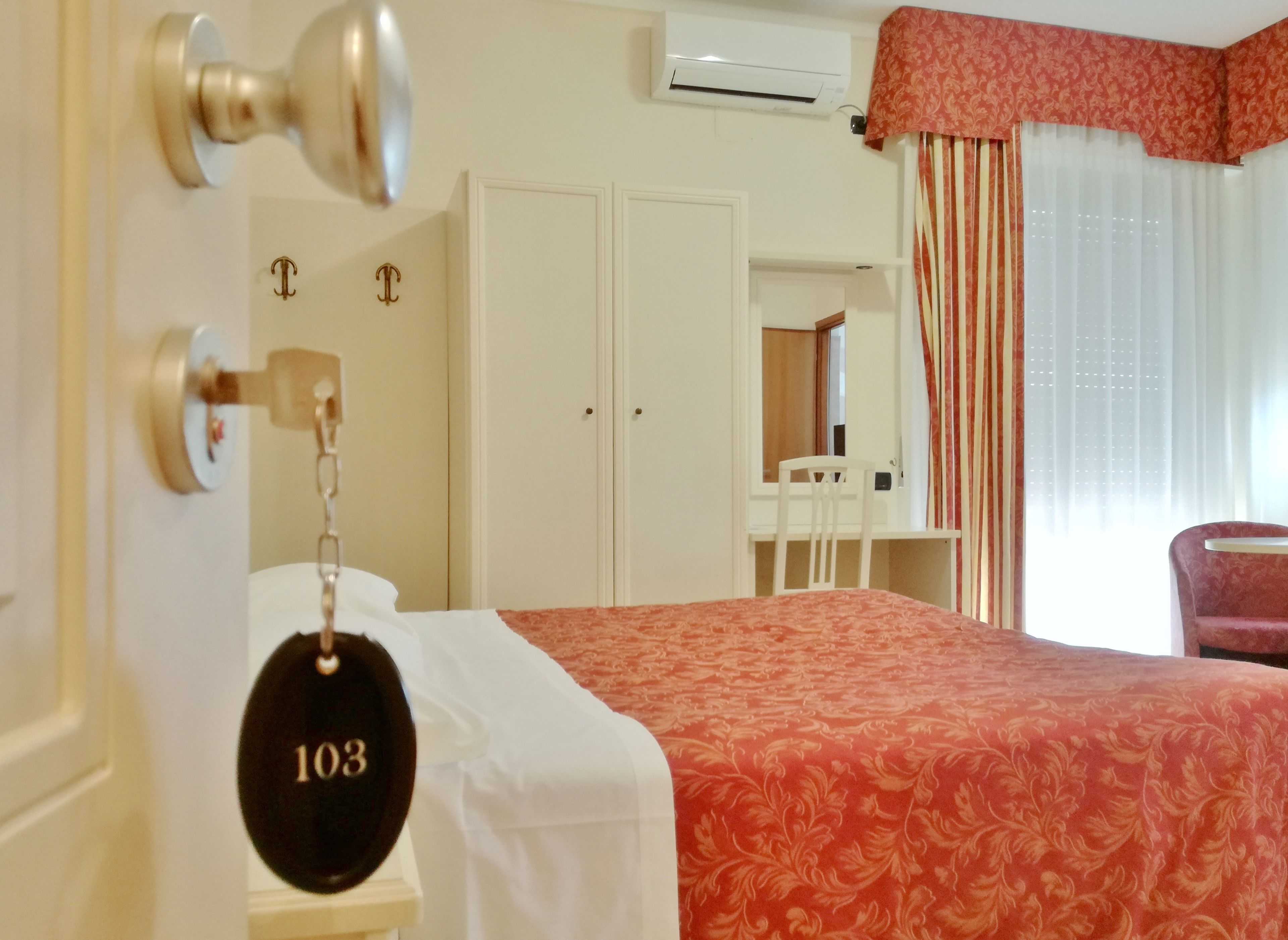 A hotel room with a bed, a desk, a chair, and a wardrobe.
