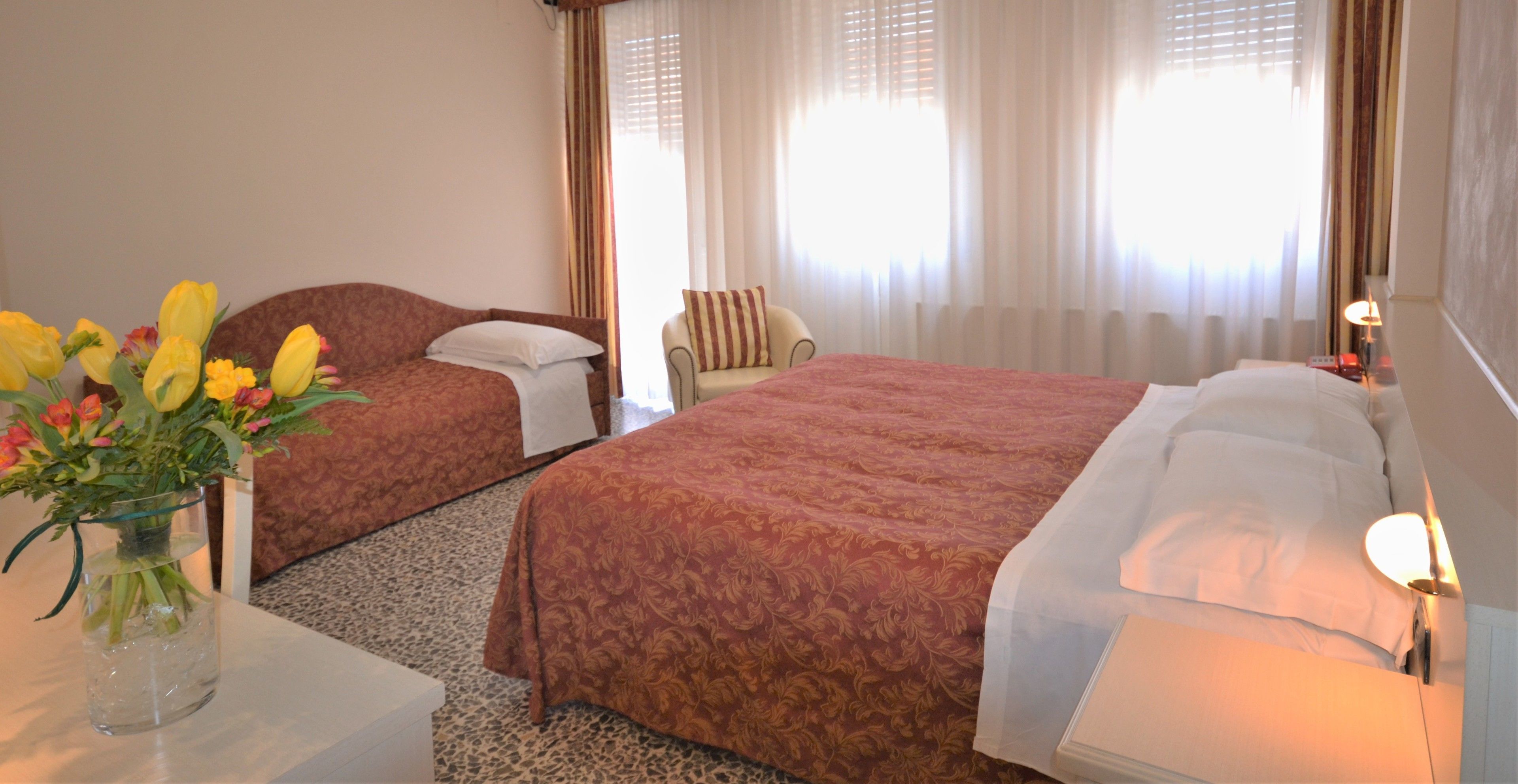 A hotel room with two beds, a sitting area, and a vase of flowers on a table.