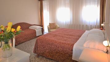 A hotel room with two beds, a sitting area, and a vase of flowers on a table.