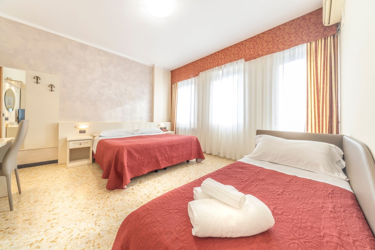 Quarto de hotel com duas camas, uma escrivaninha e um espelho.