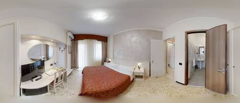 A bedroom with a bed, bedside tables, a desk with a chair, a mirror, and a bathroom visible through an open door.