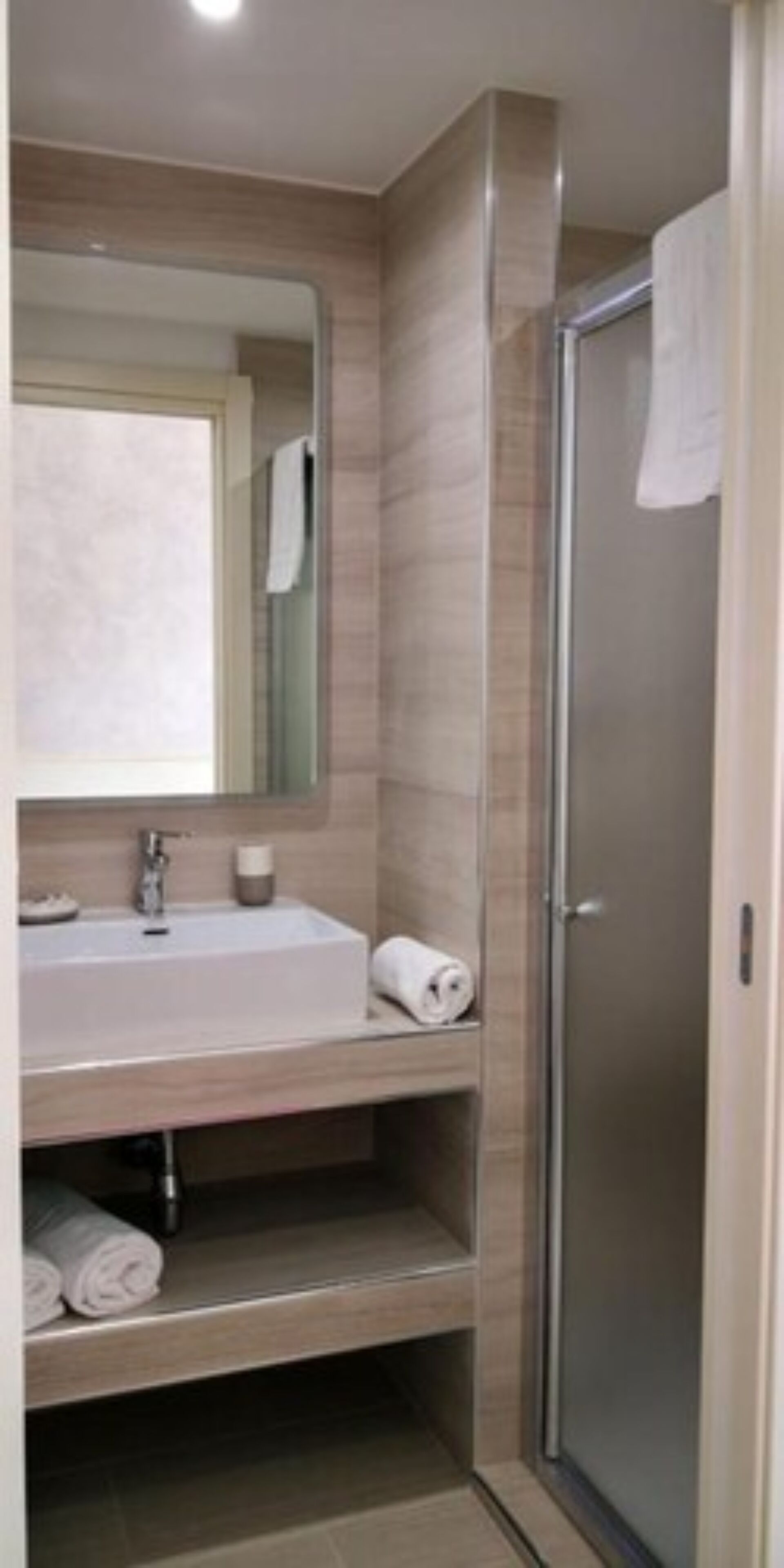 Un baño moderno con cabina de ducha de vidrio, un lavabo con espejo y un perchero para toallas.