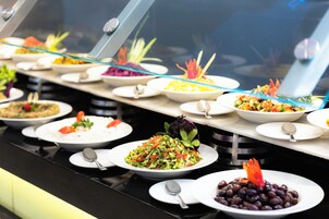 Un bufé con diversos platos, como ensaladas, arroz y frijoles, dispuestos en una barra.