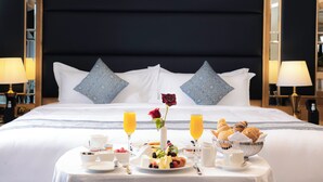 A neatly made breakfast table with a variety of foods, a vase with a single red rose, and two glasses of orange juice on a bed with a dark headboard and matching pillows. - MADEN Hotel-مادن (Madinah)