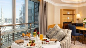 A hotel room with a dining area, breakfast buffet, and a view of a cityscape. - MADEN Hotel-مادن (Madinah)