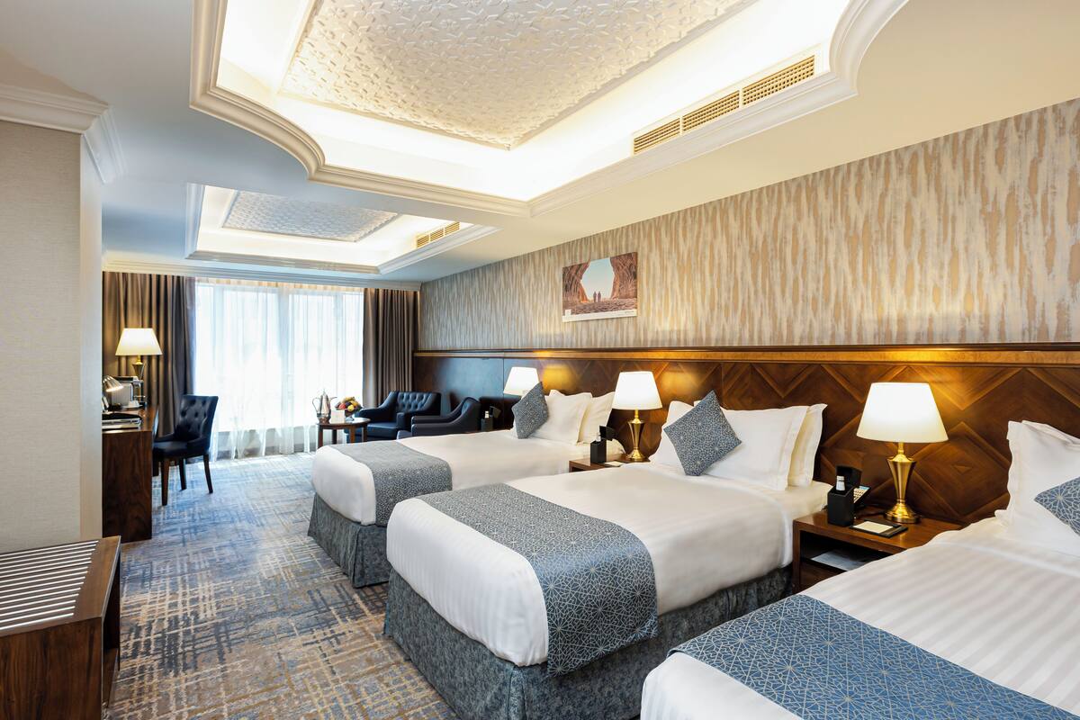 A hotel room with three beds, a desk, a chair, and a large window.