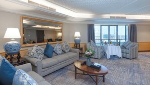 A hotel room with a large window, a sofa, a coffee table, and a dining table set for two. - MADEN Hotel-مادن (Madinah)