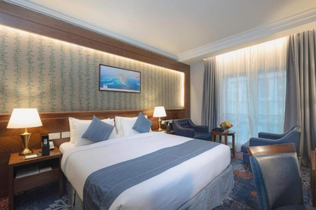 A hotel room with a large bed, two bedside tables with lamps, a small table with a vase, and a chair.