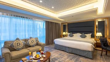 A hotel room with a large bed, a sofa, a coffee table with breakfast items, and a view through the window.