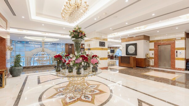 A lobby with a glass table centerpiece, a chandelier, and a reception desk. - MADEN Hotel-مادن (Madinah)