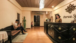 A reception area with a black reception desk, a statue, and a person seated on a bench. - Porwa House (Chiang Mai)