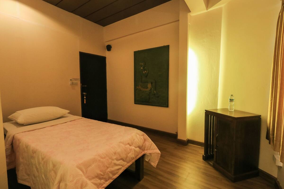 A bedroom with a bed, a nightstand, a painting on the wall, and a door.
