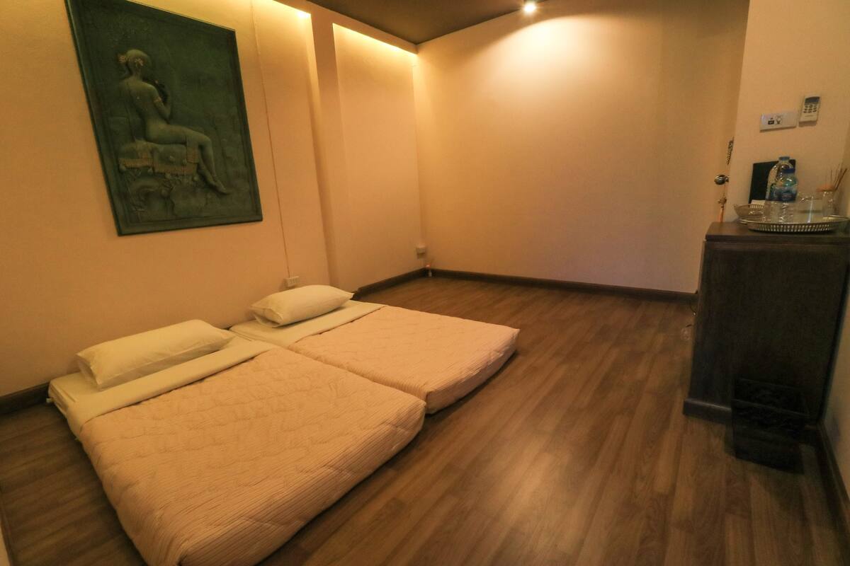 A hotel room with two single beds, a wooden floor, a painting on the wall, and a small table with a tray.