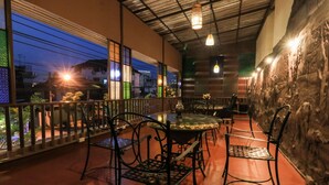 An indoor balcony with a round table and chairs, a view of the cityscape at dusk, and a stone wall on one side. - Porwa House (Chiang Mai)