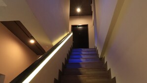 A wooden staircase with a modern light fixture on the left side. - Porwa House (Chiang Mai)