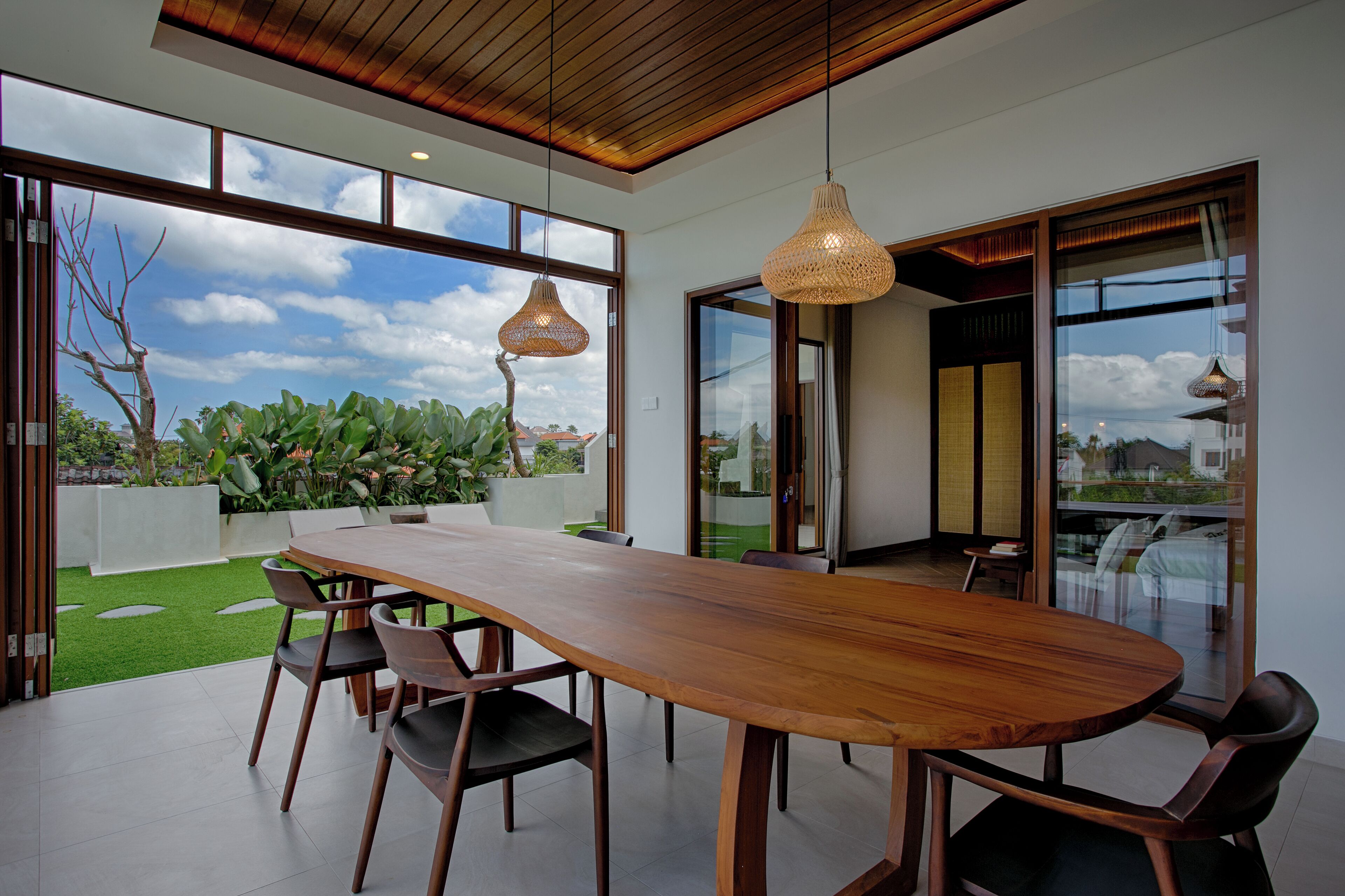 A spacious dining area with a long wooden table and chairs, large windows, and hanging light fixtures.