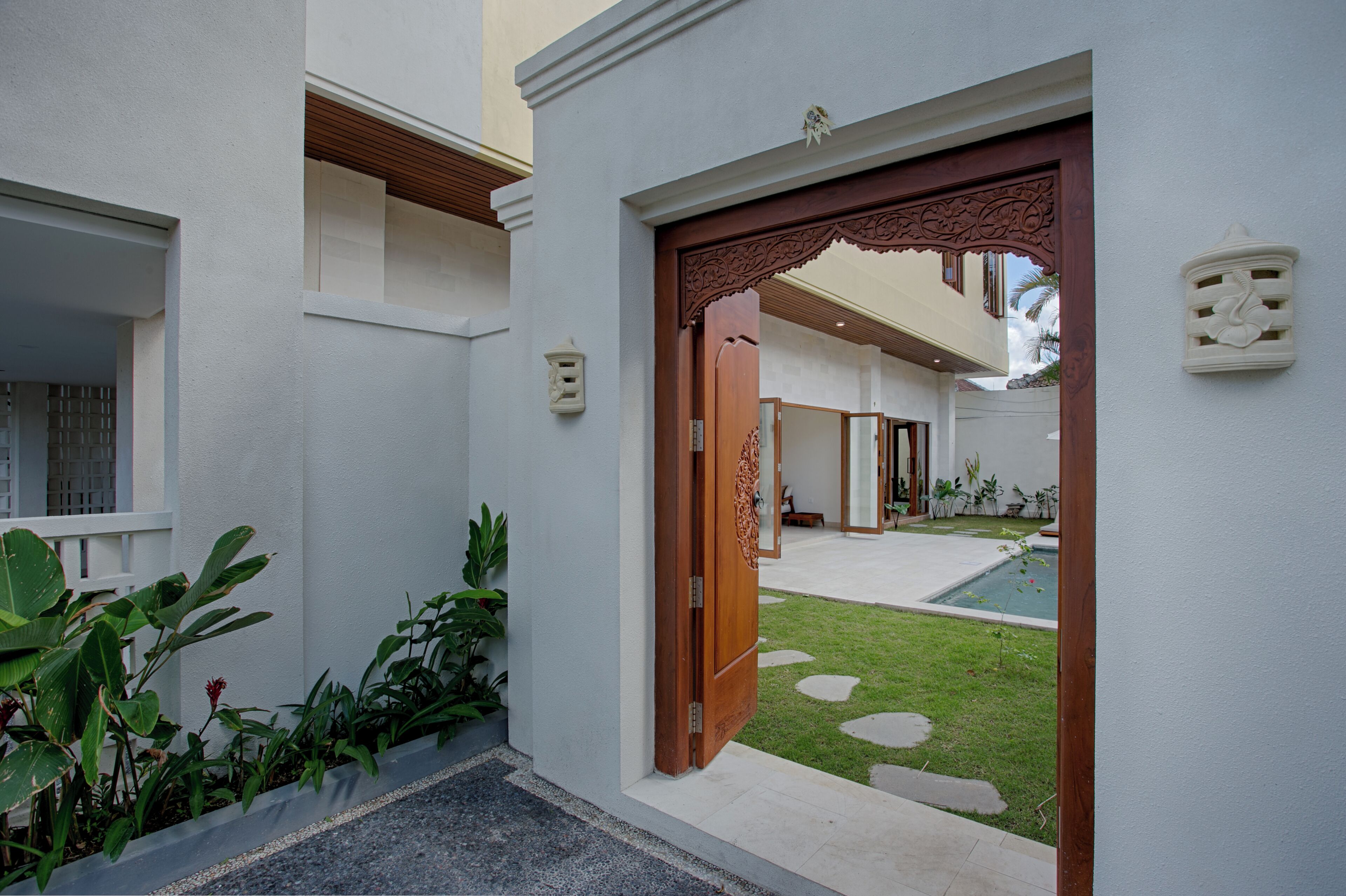 Un edificio moderno con una porta in legno, un piccolo giardino e una piscina.