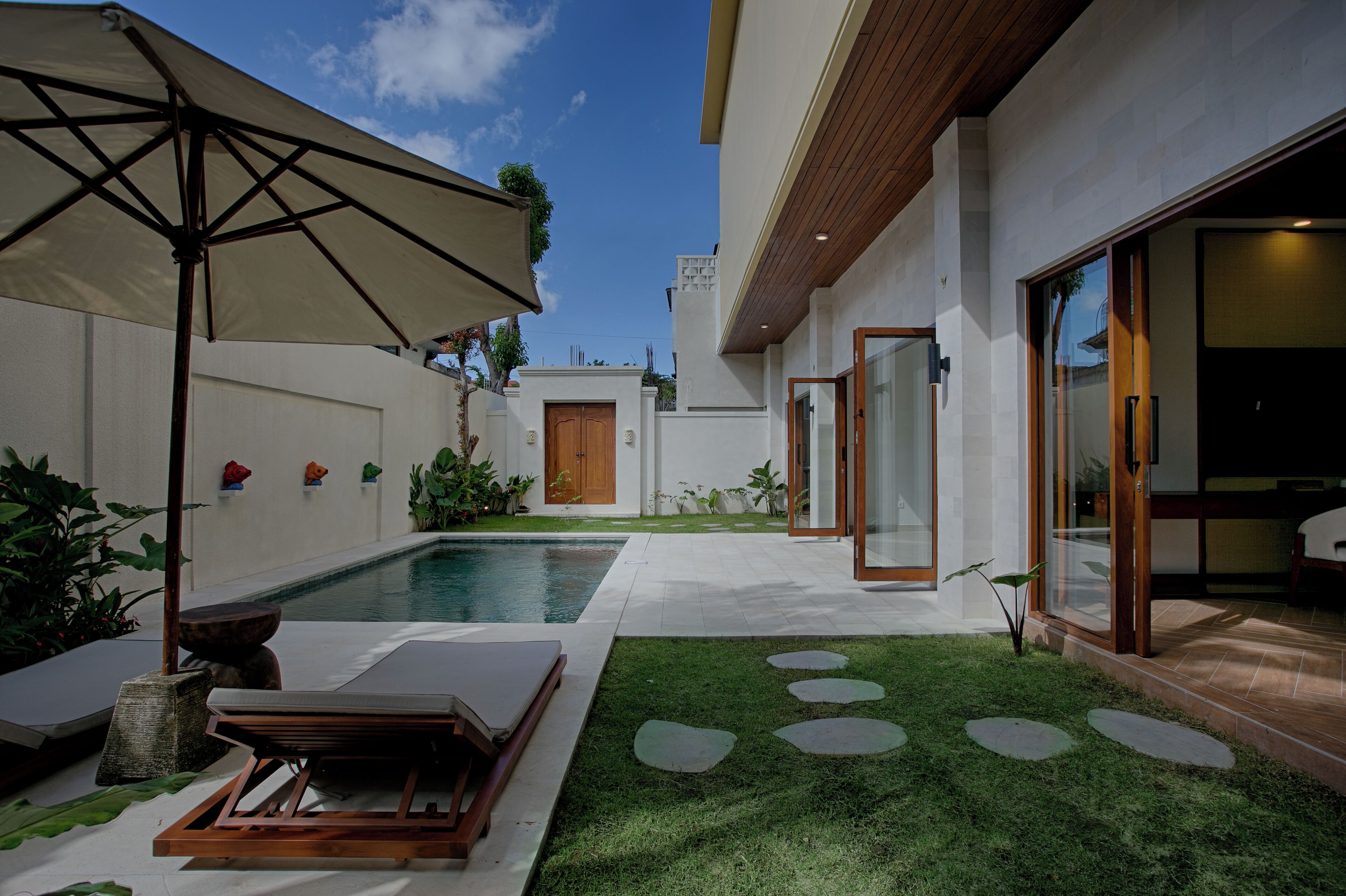 A modern outdoor pool area with a lounge chair and umbrella, surrounded by a well-maintained lawn and a small garden.