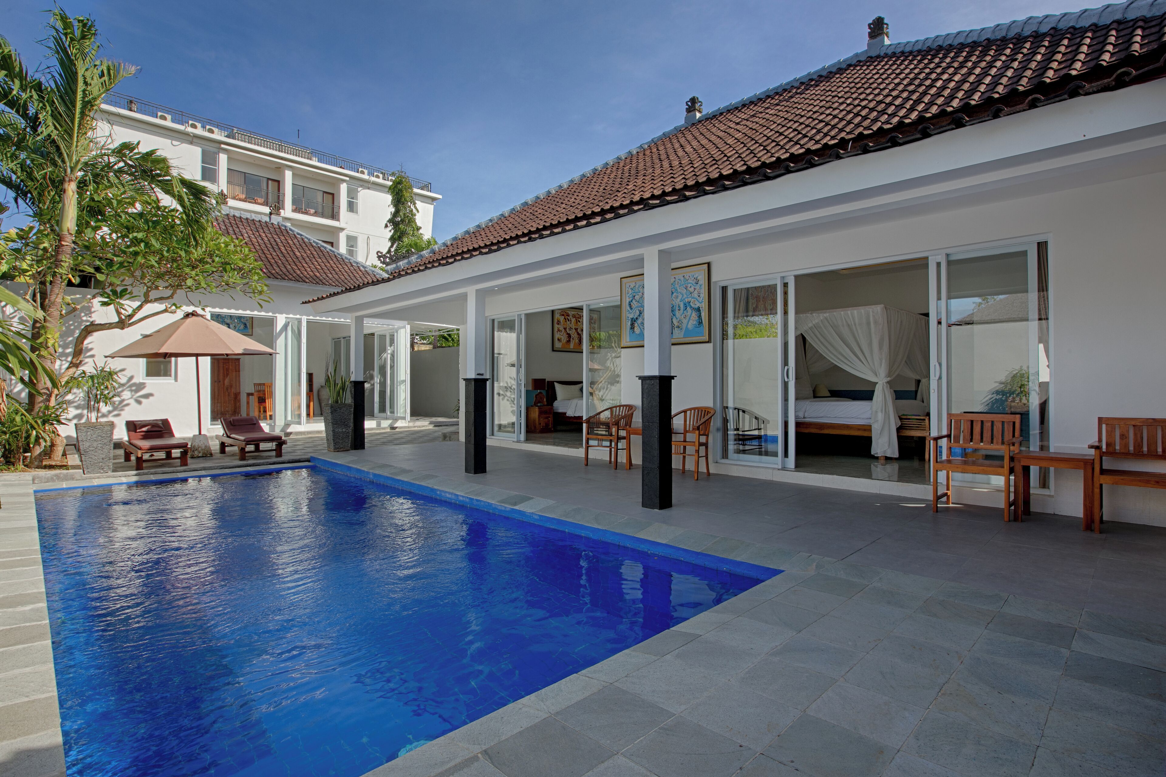 Una piscina con sillones de descanso, un porche cubierto y un dormitorio con cama y cortinas.