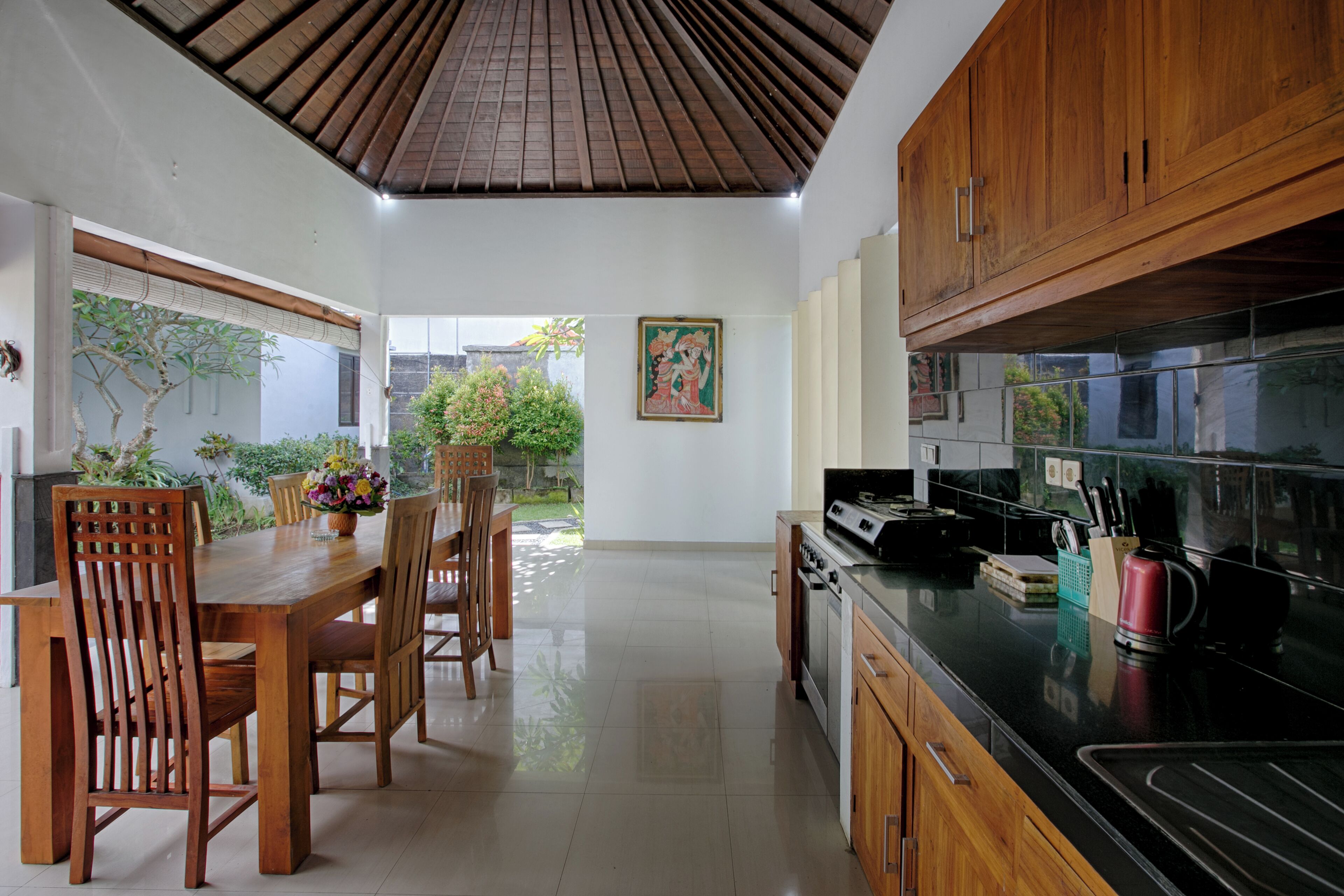 A modern kitchen with wooden cabinets, a black countertop, and a dining area with wooden chairs and a table.