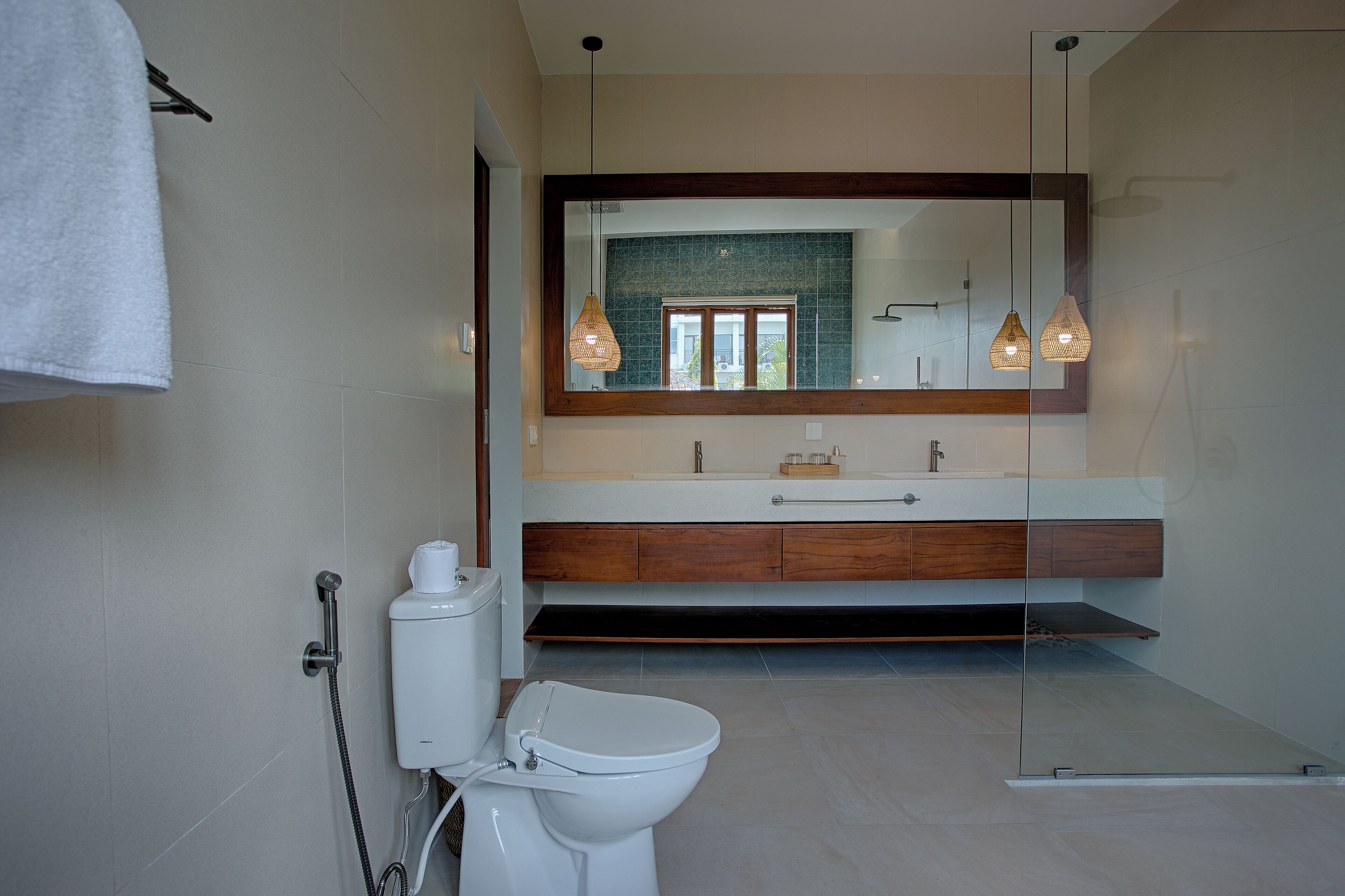 A modern bathroom with a glass shower enclosure, a white toilet, and a large mirror above a wooden vanity.