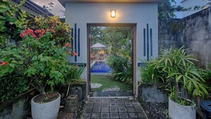 A modern entrance with a light fixture, a pathway leading to a pool area, and potted plants on either side.