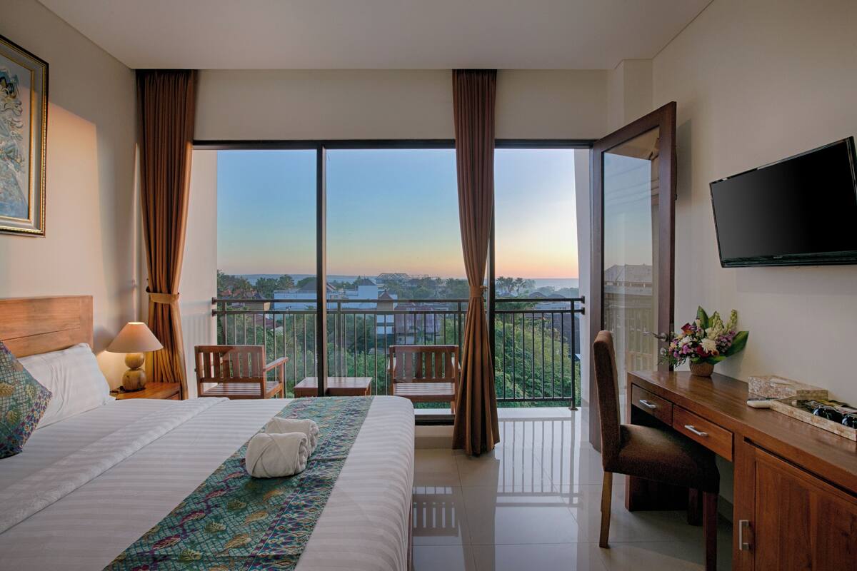 Une chambre d’hôtel avec un grand lit, un bureau doté d’une télévision à écran plat, un balcon avec vue et un tableau au mur.