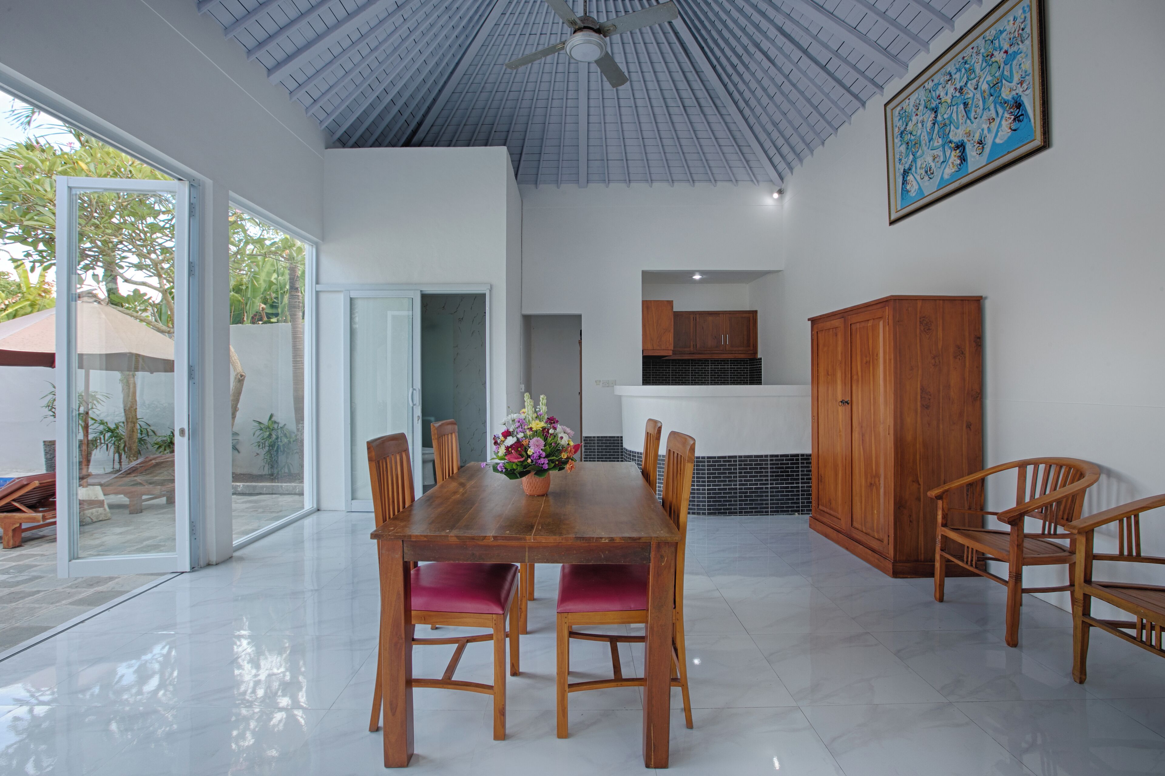 A spacious dining area with a wooden table and chairs, a ceiling fan, and a view through large glass doors.
