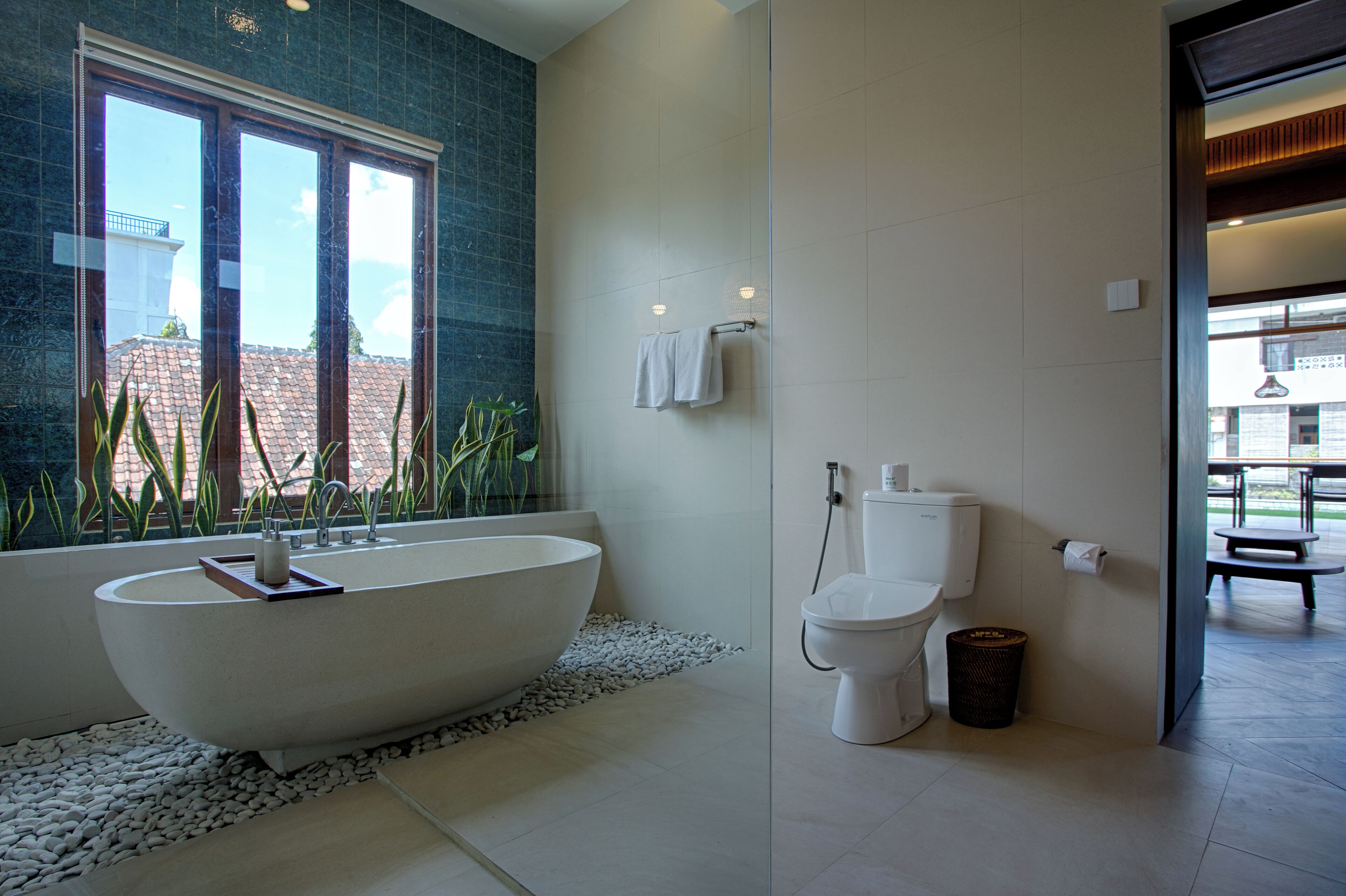A modern bathroom with a freestanding bathtub, a toilet, and a window with a view of buildings.
