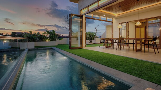 A modern house with a swimming pool, glass doors, and a dining area.