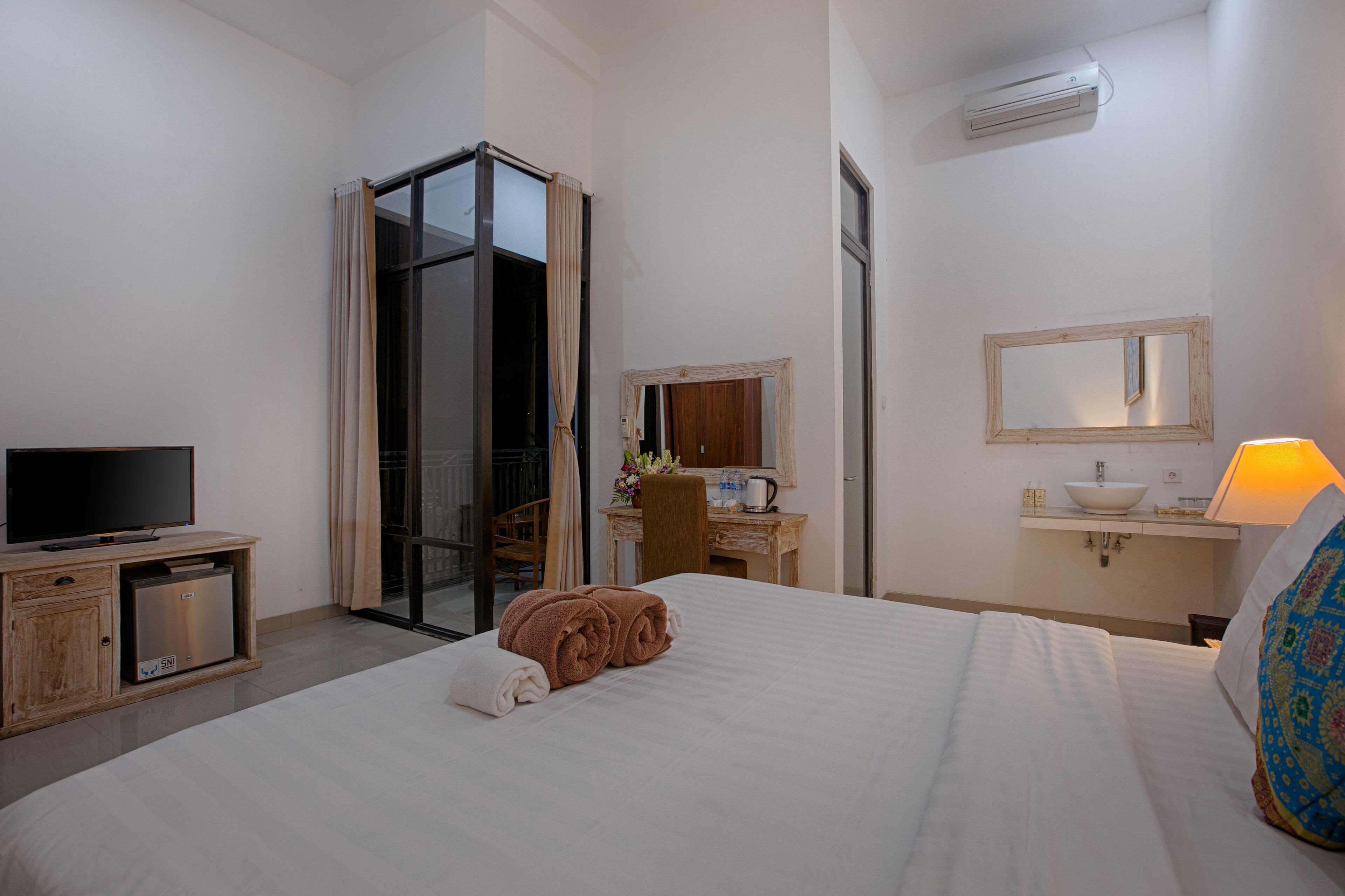 Una habitación de hotel con cama, televisión, escritorio, espejo y lavamanos.