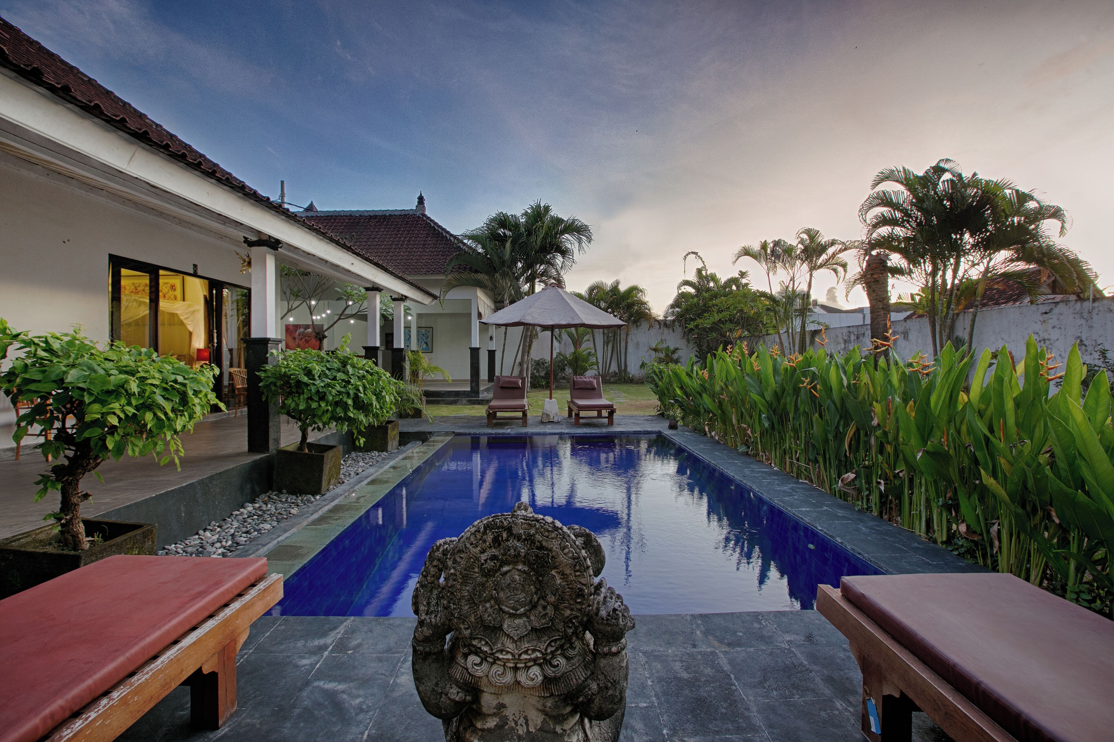 A serene pool area with a statue, benches, and lush greenery.