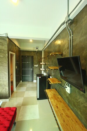 A modern hotel room with a flat-screen TV mounted on the wall, a wooden bench, and a red sofa. - Ban Suan Dokmai (Kabin Buri)