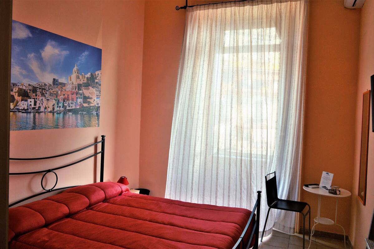 A room with a bed, a chair, a small table, and a painting on the wall.