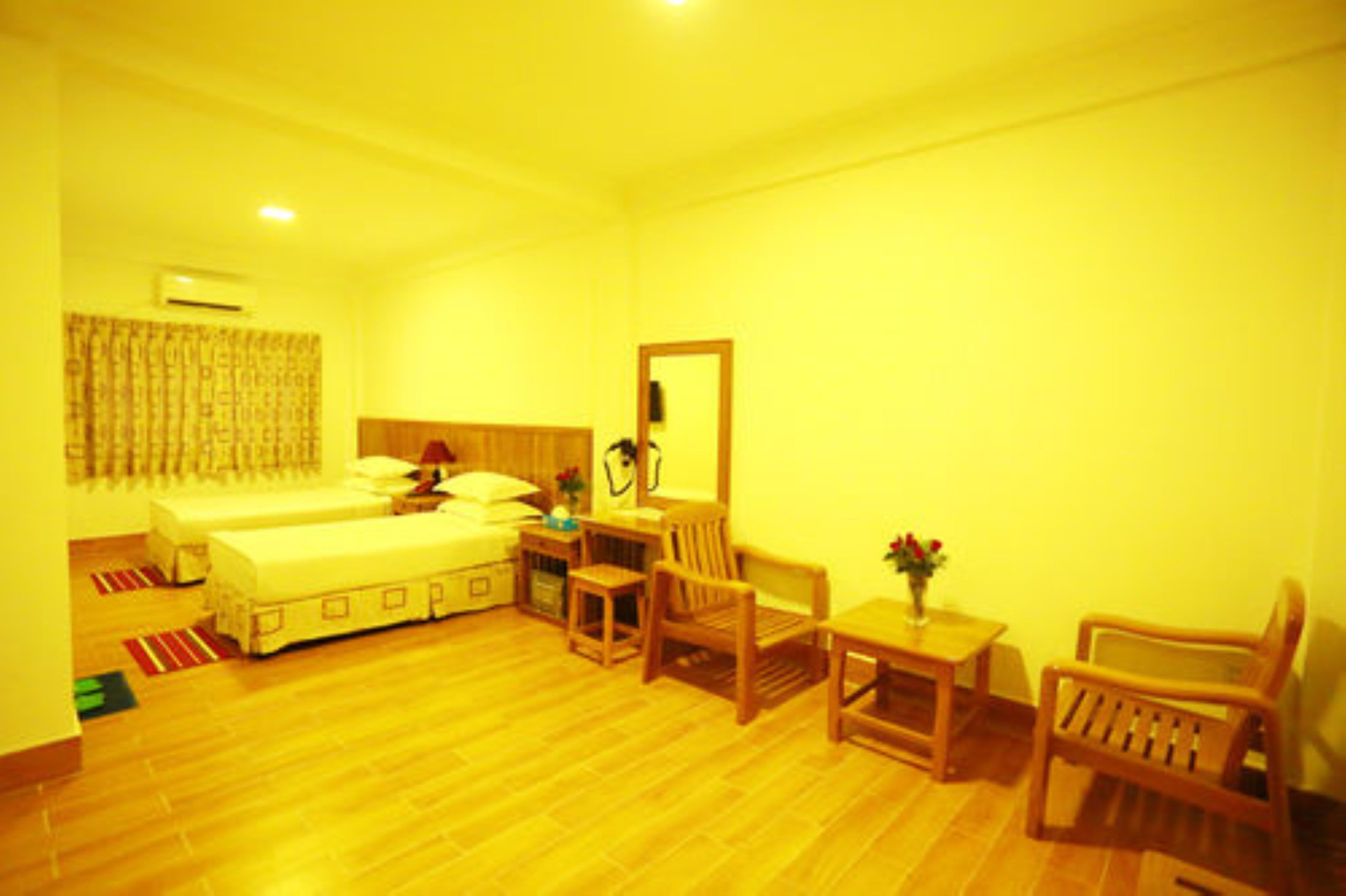 A room with two beds, a small table with a chair, a mirror, and a window with curtains.