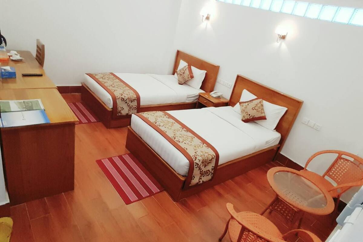 A hotel room with two beds, a desk, and a small table with chairs.