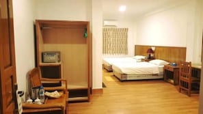 Una habitación de hotel con piso de madera, una cama con cabecera, un escritorio con silla, una mesita de noche con lámpara y un armario.