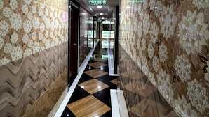 Um corredor com paredes estampadas, piso xadrez e uma placa indicando o caminho para a recepção.