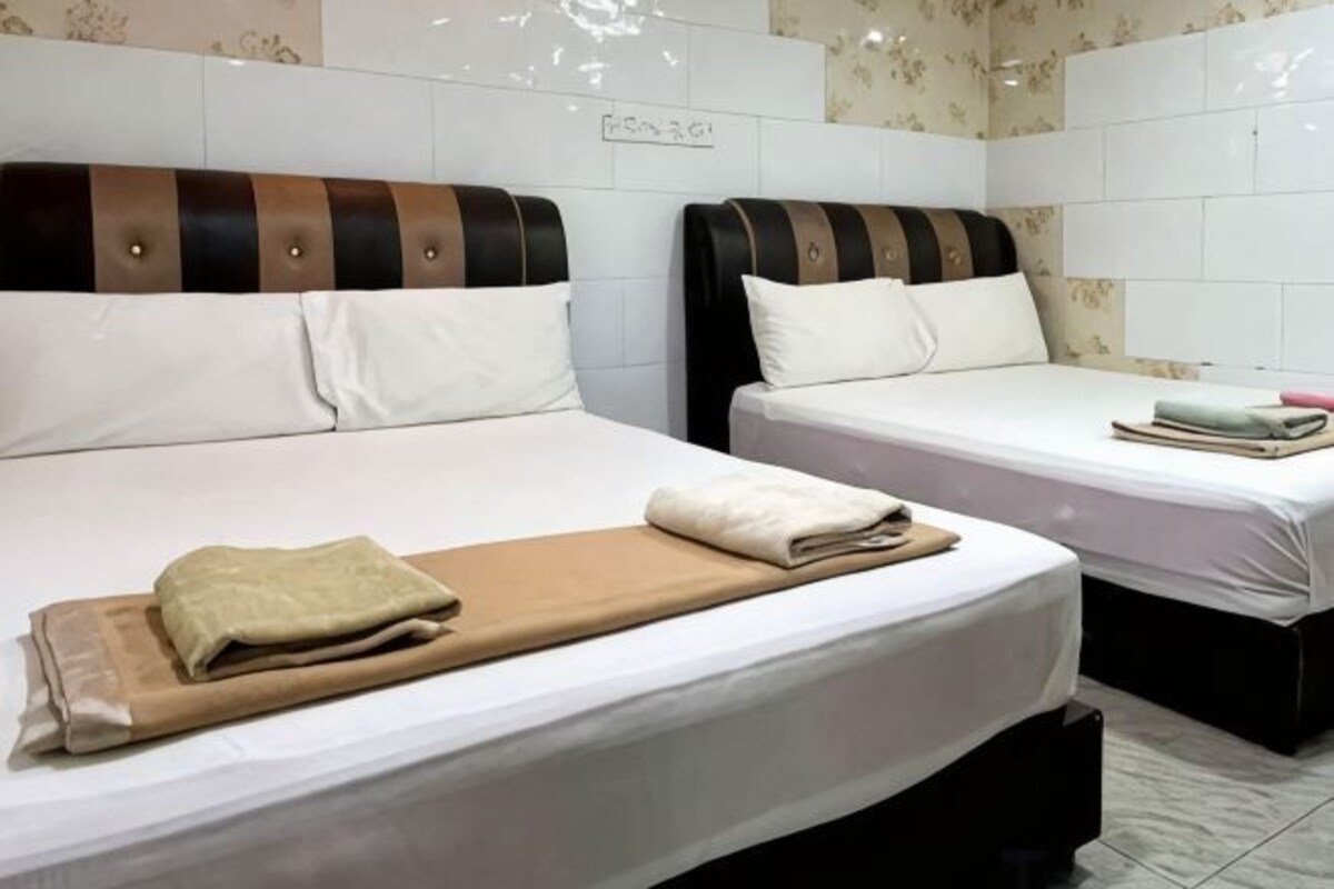 Two single beds with white linens, a brown blanket, and a small bedside table with a book and a pink item.