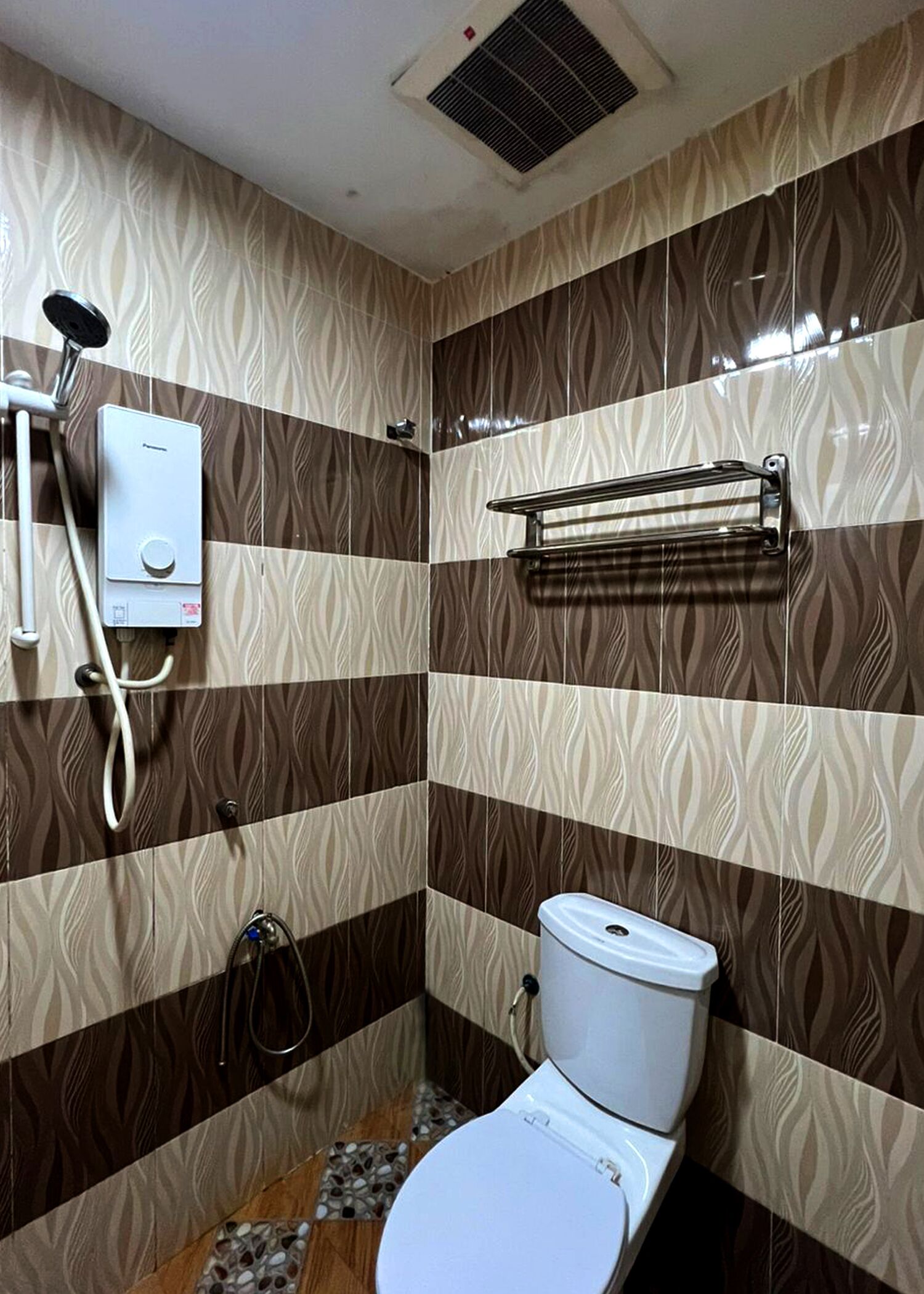 Une salle de bain avec des carreaux décorés, des toilettes, une douche et un porte-serviettes.