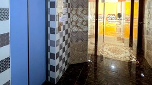 Um hall de hotel com um padrão quadriculado na parede, um elevador azul e piso de mármore.
