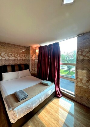 Habitación de hotel con una cama grande, una ventana con cortinas y vistas al exterior.