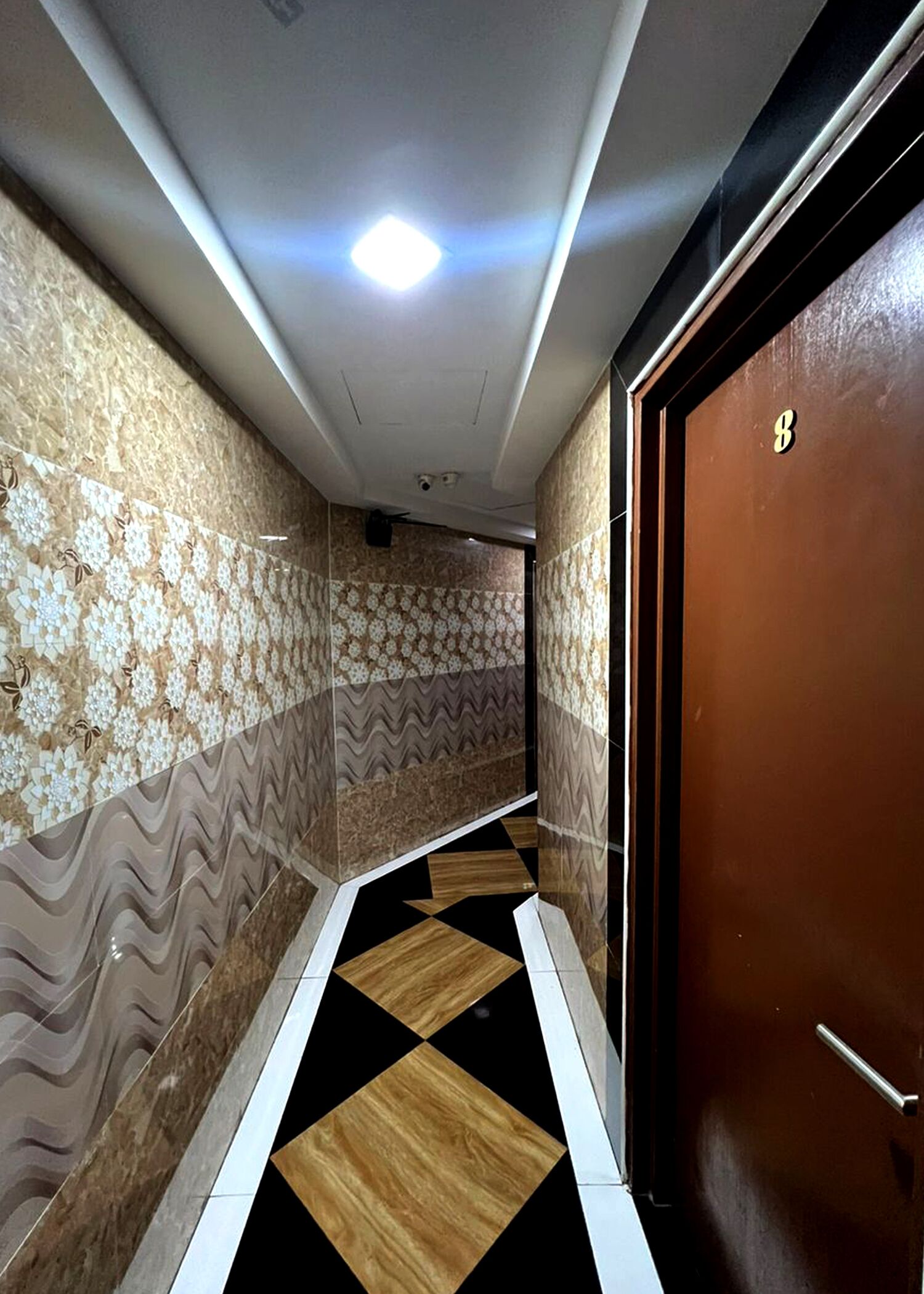 A hallway with patterned walls, a black and white tiled floor, and a brown door with a 'B' marking.