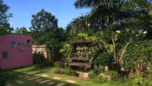 A garden with a small pink building, a wooden pergola, and a stone pathway. - Banana Place Resort (Chumphon)