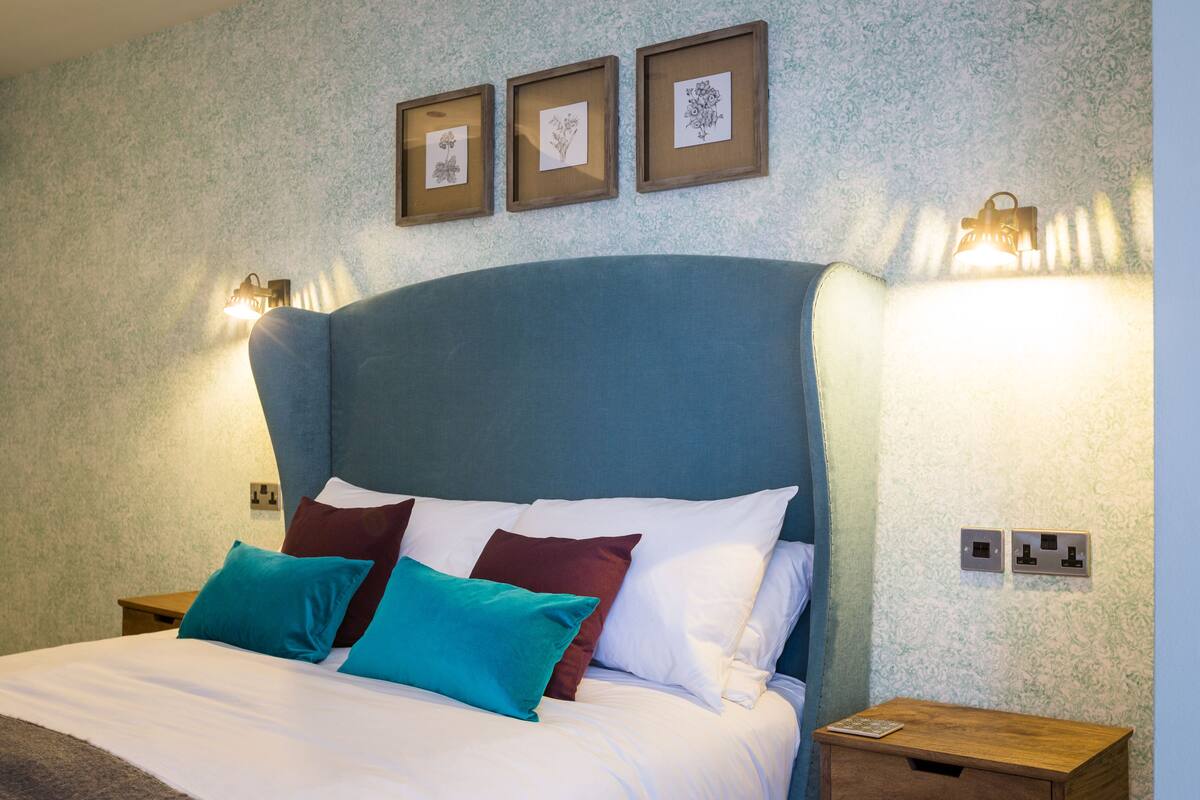 A neatly made bed with white and teal pillows, a blue headboard, and wall-mounted light fixtures.