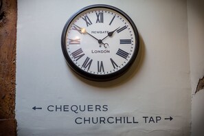 A wall-mounted clock with Roman numerals and the words "NEWGATE LONDON" on it. Below the clock, there are directional arrows pointing to "CHEQUERS" and "CHURCHILL TAP". - The Chequers Marlow (Marlow)